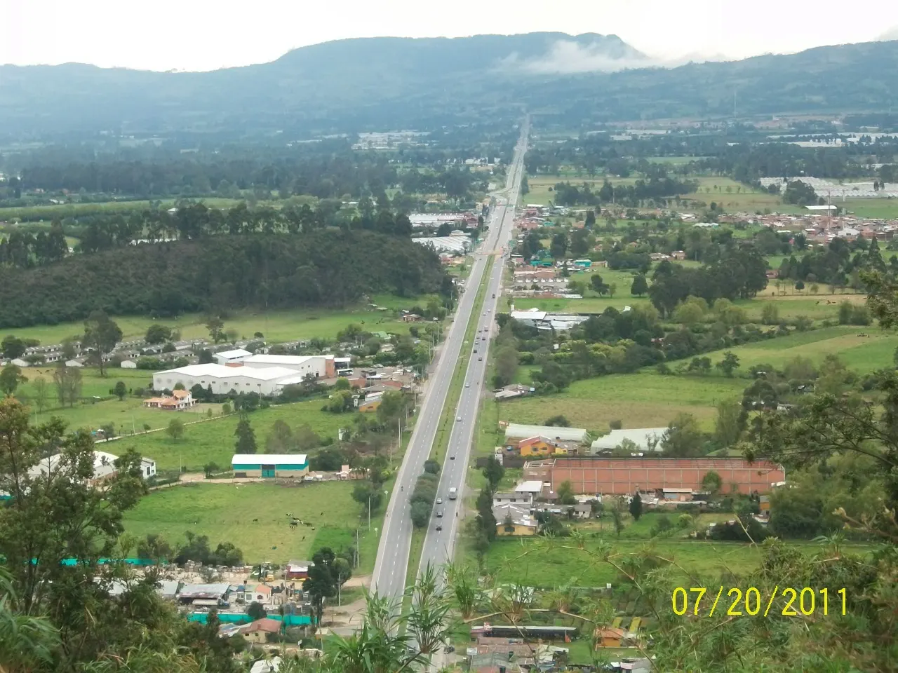 Vista aérea de un tramo recto de la autopista Medellín-Bogotá entre potreros y casas